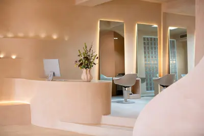 A curved plaster reception desk lit by wall niches, with styling chairs and backlit mirrors on the floor beyond