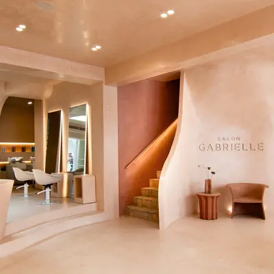 The Hawksburn salon looking through to the styling floor, with a curved staircase and Salon Gabrielle lettering on a terracotta wall