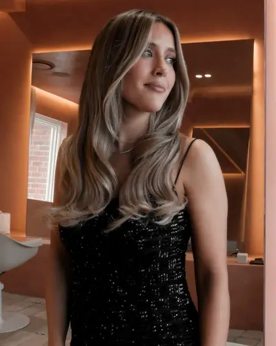 Woman in a black sequinned slip dress in the salon, hair in long glossy waves with bright blonde face-framing pieces